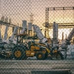 An industrial power plant with heavy machinery and equipment behind a chain link fence during sunset, showcasing energy infrastructure.
